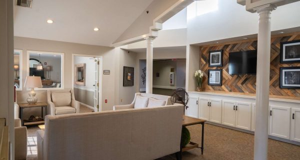Bright neutral-toned lounge with beige sofas, accent wood-paneled wall, TV, columns and soft ambient lighting.