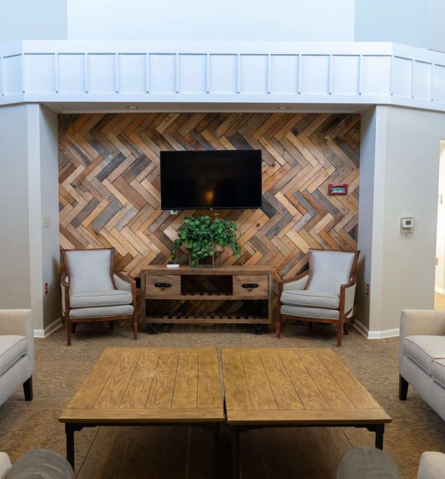 Cozy living room with herringbone wood accent wall, wall-mounted TV, neutral sofas, wooden coffee table, and armchairs