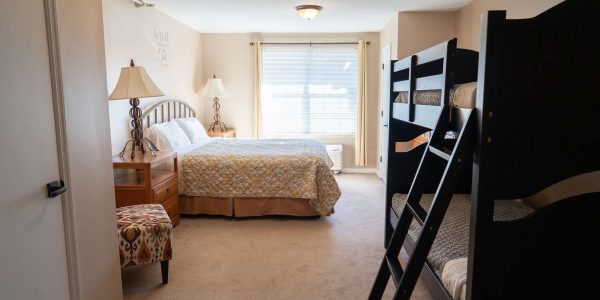 Bright family bedroom with queen bed, dark wooden bunk beds, nightstands and lamps, window with blinds