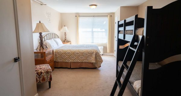 Bright family bedroom with queen bed, dark wooden bunk beds, nightstands and lamps, window with blinds